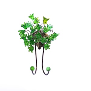 Könnte beinhalten: Ein dekorativer Wandhaken in Form eines Baumes mit grünen Glasblättern und einer braunen Holzbasis. Der Haken hat zwei Metallarme mit grünen Glaskugeln an den Enden.