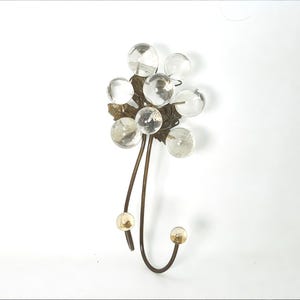 Könnte beinhalten: Ein goldfarbener Haken aus Metall mit einer Gruppe von durchsichtigen Glaskugeln, die oben angebracht sind. Die Kugeln sind in Form einer Blume angeordnet.
