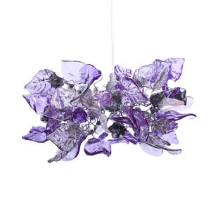 Op de afbeelding: Een decoratieve kroonluchter met een bloemenontwerp. De armatuur heeft doorschijnende paarse en zilveren glazen bloemblaadjes en bladeren, opgehangen aan een draadframe. De lamp hangt aan een wit snoer tegen een witte achtergrond.