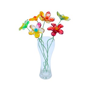 May include: A bouquet of colorful glass flowers in a clear glass vase. The flowers are red, orange, yellow, and green.