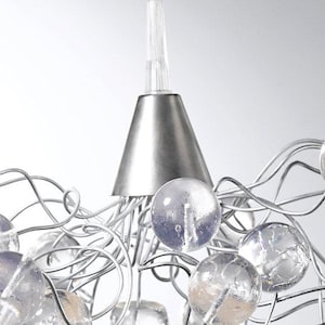 May include: Close-up of a modern chandelier with a silver metal cone and clear glass orbs. The orbs are connected by silver wires, creating a unique and elegant lighting fixture. The design is contemporary.