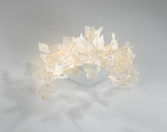 May include: A white glass sculpture with a square base and multiple organic shapes, resembling a cluster of flowers or leaves.