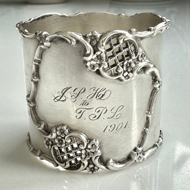 This is an antique sterling silver napkin ring with lovely acanthus leaf designs and original patina.  Open basket weave and  forget-me-not florals.  Engraved JPH to TPL 1901.  Signed Sterling and hallmarked.   Wonderful antique condition.