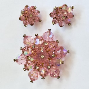Peut inclure: Un ensemble de bijoux composé d'une grande broche circulaire et de deux boucles d'oreilles circulaires assorties. Chaque pièce présente des perles en cristal rose clair à facettes disposées en motif floral avec des strass dorés.