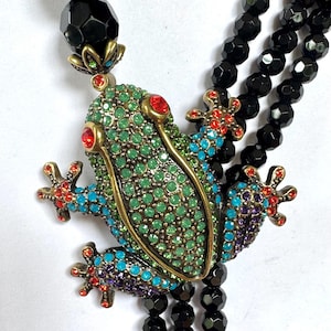 May include: A colorful frog pendant necklace with a beaded chain. The frog is embellished with green, blue, red, and purple rhinestones. The necklace features a black faceted bead chain and a large black bead at the top.
