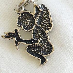 May include: A silver-toned pendant necklace featuring a detailed angel design. The angel is depicted in a seated pose, holding a sprig. The pendant has a textured, oxidized finish, and is suspended from a delicate chain.