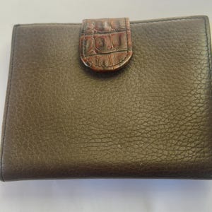 Puede incluir: Una cartera de cuero marr&oacute;n con una superficie texturizada. La cartera tiene forma rectangular con un cierre de solapa de piel de cocodrilo sint&eacute;tica marr&oacute;n. La cartera est&aacute; cerrada.