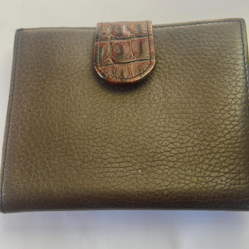 Puede incluir: Una cartera de cuero marr&oacute;n con una superficie texturizada. La cartera tiene forma rectangular con un cierre de solapa de piel de cocodrilo sint&eacute;tica marr&oacute;n. La cartera est&aacute; cerrada.