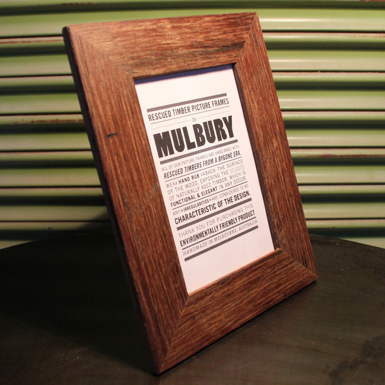 May include: A rustic brown wooden picture frame with a white paper insert. The paper has black text that reads "Rescued Timber Picture Frames by Mulbury. All of our picture frames are handmade with rescued timbers from a bygone era. We hand rub back the surface of the wood, exposing the naturally aged timber, which is functional & elegant in any decor. Any irregularities are considered to be characteristic of the design. Thank you for purchasing this environmentally friendly product. Handmade in Melbourne, Australia."