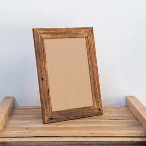 May include: A rustic wooden picture frame with a brown cardboard insert. The frame has a natural wood finish with knots and grain visible. It is sitting on a wooden surface.
