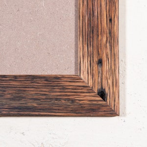 May include: A close-up of the corner of a dark brown wooden picture frame. The frame has a natural wood grain and a distressed finish.