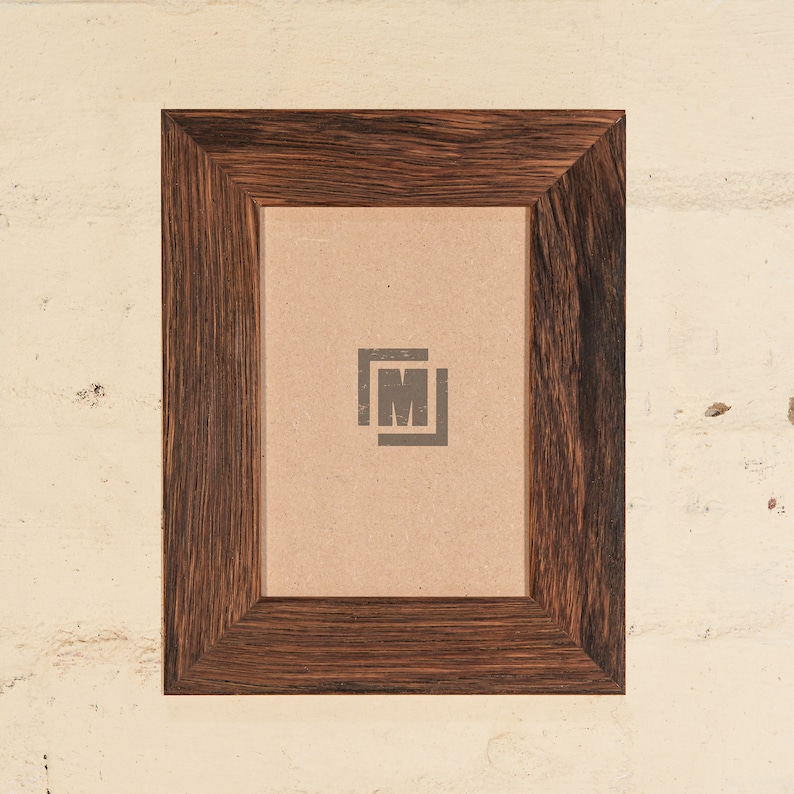 May include: A dark brown wooden picture frame with a light brown mat and a small logo in the center. The frame is approximately 8 inches by 10 inches.