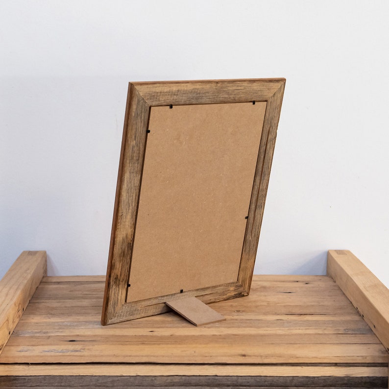 May include: A rustic wooden picture frame with a brown cardboard backing. The frame has a stand on the back and is made of reclaimed wood.