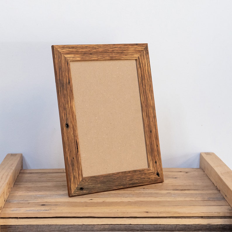 May include: A rustic wooden picture frame with a brown cardboard insert. The frame has a natural wood finish with knots and grain visible. It is sitting on a wooden surface.