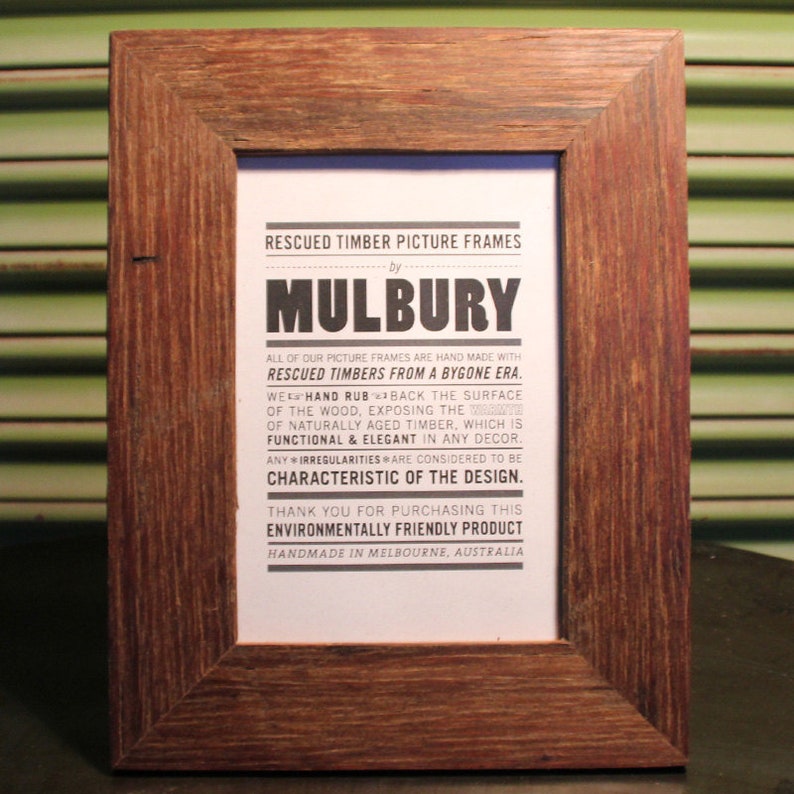 May include: A rustic wooden picture frame with a sign that reads "Rescued Timber Picture Frames by Mulbury. All of our picture frames are hand made with rescued timbers from a bygone era. We hand rub back the surface of the wood, exposing the ... of naturally aged timber, which is functional & elegant in any decor. Any irregularities are considered to be characteristic of the design. Thank you for purchasing this environmentally friendly product. Handmade in Melbourne, Australia."