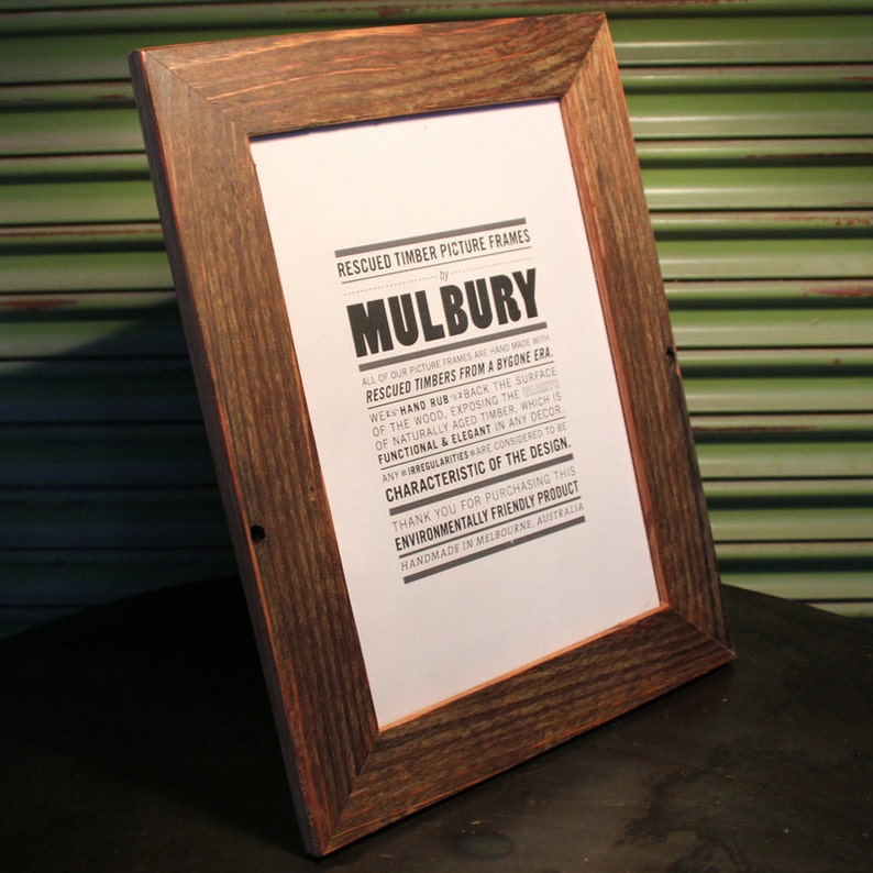 May include: A rustic wooden picture frame with a natural wood finish. The frame is made from reclaimed timber and features a sign that reads "Rescued Timber Picture Frames by Mulbury". All of our picture frames are hand made with rescued timbers from a bygone era. We hand rub back the surface of the wood, exposing the naturally aged timber, which is functional & elegant in any decor. Any irregularities are considered to be characteristic of the design. Thank you for purchasing this environmentally friendly product. Handmade in Melbourne, Australia.