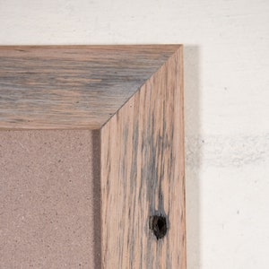 May include: Close-up of the corner of a rustic wooden frame with a light brown and gray wood grain. The frame has a knot hole and is surrounding a corkboard.