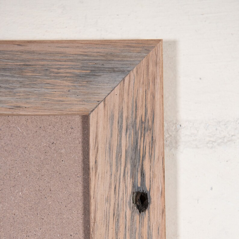 May include: Close-up of the corner of a rustic wooden frame with a light brown and gray wood grain. The frame has a knot hole and is surrounding a corkboard.