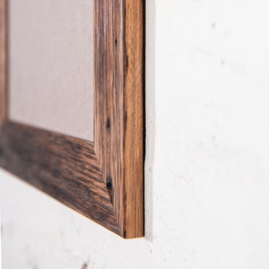 May include: Close-up of a wooden picture frame with a dark brown stain. The frame has a rustic look with visible wood grain and knots.