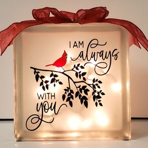 May include: A glass block with a red cardinal perched on a branch with leaves. The block is illuminated with white lights and has the text "I am always with you" written in black cursive.