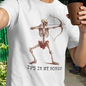 May include: White t-shirt with a skeleton archer graphic and the text "IT'S IN MY BONES".