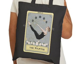 Puede incluir: Bolsa de tela negra con una ilustración amarilla y blanca de una mujer haciendo una pose de pilates. La ilustración está en el estilo de una carta de tarot con el texto "The Pilates" y "XXXVII" en la carta.