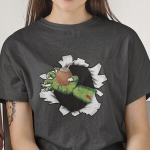 May include: A dark gray t-shirt with a graphic of a green zombie hand reaching out of a ripped hole, holding a brown and green mate gourd.