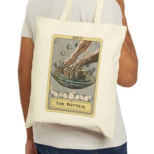 May include: A beige tote bag with a tarot card design. The card is titled "The Potter" and depicts a pair of hands shaping clay on a pottery wheel. The card is surrounded by a decorative border with floral elements.