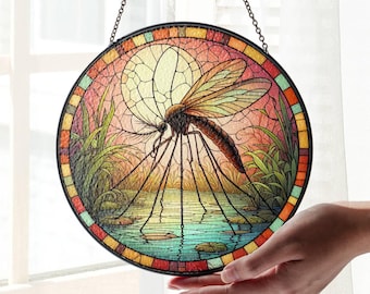 May include: A stained glass window hanging from a chain. The window is round and features a colourful image of a large mosquito with long legs standing in a pond with lily pads. The background is a sunset with a large moon.