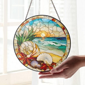 Puede incluir: Una ventana redonda de vidrio coloreado que cuelga de una cadena. La ventana representa una concha, una escena de playa y una puesta de sol. Los colores son azul, verde, amarillo, naranja y blanco.