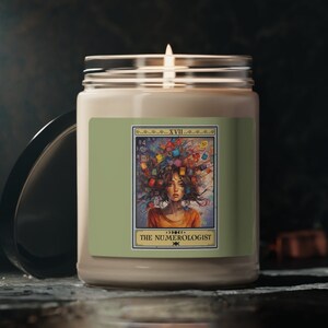 May include: A white candle with a green label featuring a woman with colorful numbers surrounding her head. The label reads "XVIII THE NUMEROLOGIST".
