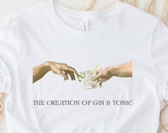 May include: White t-shirt with a graphic of two hands reaching towards each other, one holding a glass of gin and tonic. The text "THE CREATION OF GIN & TONIC" is printed below the graphic.