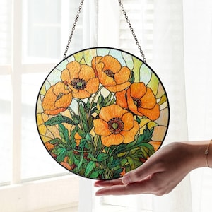 May include: A stained glass window hanging on a chain, featuring a cluster of orange poppies with green leaves and stems. The window is round and has a dark brown frame.