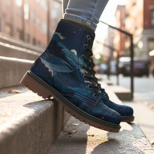 May include: Blue combat boots with a whale and ocean design. The boots feature a dark blue background with a whale, waves, and a moon. The boots have black laces and brown soles.