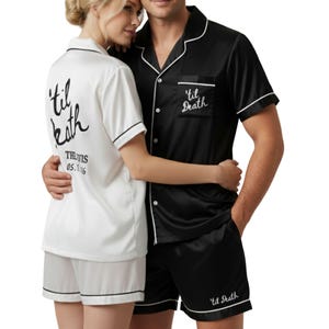 Puede incluir: Conjuntos de pijama de satén a juego en blanco y negro. El conjunto blanco tiene "'til death" y una fecha impresa en la espalda. El conjunto negro tiene "'til death" bordado en el bolsillo y los pantalones cortos. Ambos conjuntos tienen ribetes blancos.