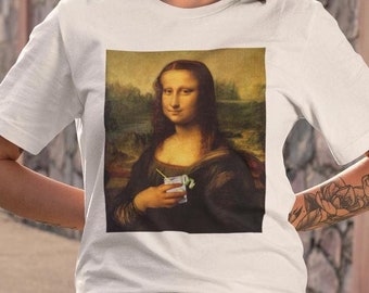 May include: White t-shirt with a print of the Mona Lisa holding a cocktail glass with a straw and a green garnish.