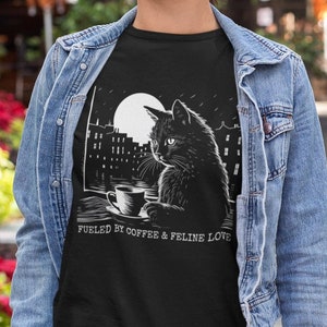 May include: Black t-shirt with a white graphic of a black cat sitting by a window with a cup of coffee. The text "Fueled by coffee & feline love" is below the image.