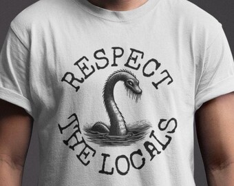 Può includere: Maglietta bianca con una grafica in bianco e nero di una creatura marina mitologica con il testo "Respect the Locals" intorno.