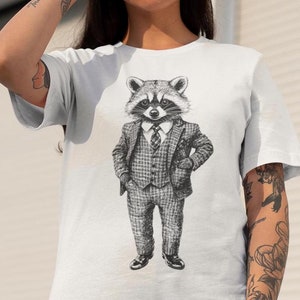 May include: White t-shirt featuring a detailed black and white illustration of a raccoon dressed in a plaid suit, tie, and dress shoes. The raccoon is standing with one hand in its pocket.