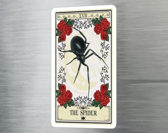 Puede incluir: Una carta de tarot vintage con una araña negra sobre un fondo blanco rodeada de rosas rojas. La carta está etiquetada como "XVII THE SPIDER".