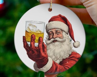 Può includere: Un ornamento natalizio rotondo in ceramica con un'illustrazione di Babbo Natale in stile cartone animato che tiene un bicchiere di whisky con cubetti di ghiaccio. Babbo Natale indossa un abito rosso con rifiniture bianche e una barba bianca.