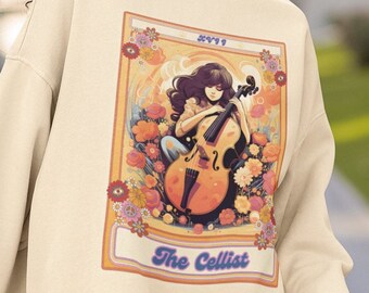 Peut inclure: Un sweat-shirt crème avec un imprimé graphique rétro d'une femme jouant du violoncelle. Le graphique est entouré de fleurs et porte le texte "The Cellist" en bas.