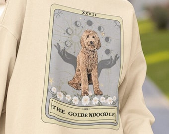 May include: A cream-colored sweatshirt with a graphic of a golden doodle dog in a tarot card design. The card reads "The Golden Doodle" and "XXXVII".