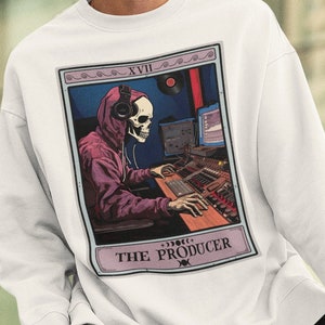 May include: White sweatshirt featuring a graphic of a skeleton wearing headphones and working on a soundboard. The graphic is in a tarot card style with the text "XVII THE PRODUCER".