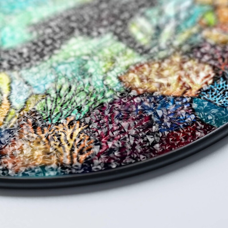 Op de afbeelding: Een ronde, zwarte dienblad met een kleurrijk moza&iuml;ekontwerp. De moza&iuml;ek is gemaakt van kleine, onregelmatige stukjes glas in tinten groen, blauw, paars, oranje en geel. De dienblad heeft een zwarte rand.