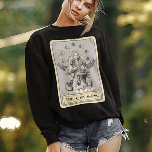K&ouml;nnte beinhalten: Schwarzer Pullover mit einem Tarotkarten-Design, das eine Frau zeigt, die von Katzen umgeben ist. Die Karte lautet "The Cat Mom".