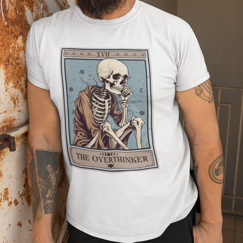 Peut inclure: T-shirt blanc avec un motif de carte de tarot repr&eacute;sentant un squelette dans une robe, avec le texte "The Overthinker" et le chiffre romain "XVII" sur la carte.
