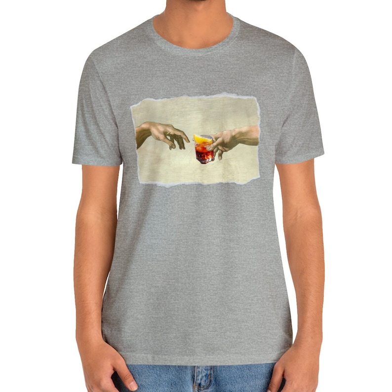 May include: A grey t-shirt with a print of two hands reaching towards each other, holding a glass of red liquid with a lemon wedge. The print is a parody of the famous "Creation of Adam" painting.