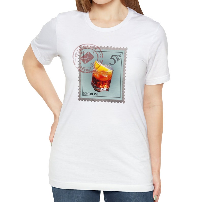 May include: White t-shirt with a vintage-style stamp design featuring a glass of Negroni with a lemon wedge. The stamp reads "5&cent;" and "NEGRONI".