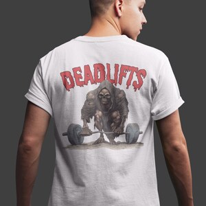 K&ouml;nnte beinhalten: Wei&szlig;es T-Shirt mit einer roten Grafik einer skelettartigen Figur, die eine Langhantel hebt. Der Text "DEADLIFTS" befindet sich &uuml;ber der Figur.